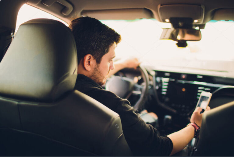 Man sitting in his car, busy using his phone to manage work tasks