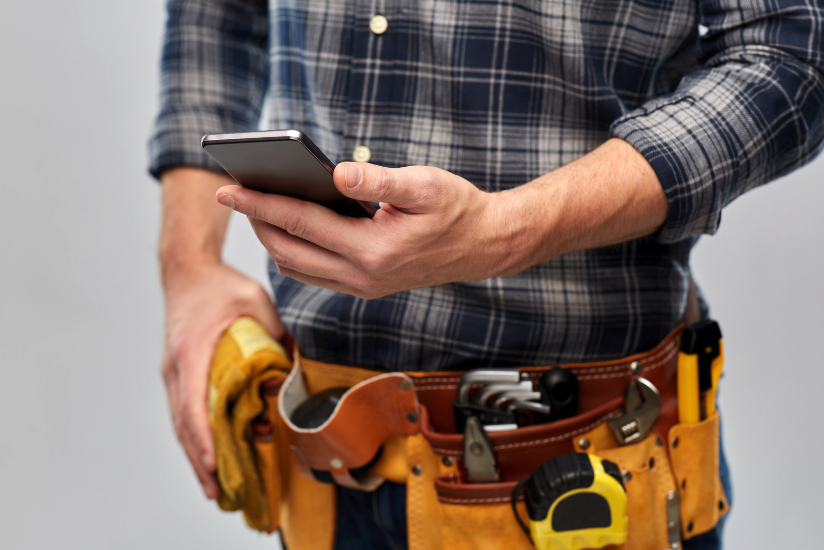 Tradie with a tool belt using a smartphone app, showcasing the best apps for tradies.